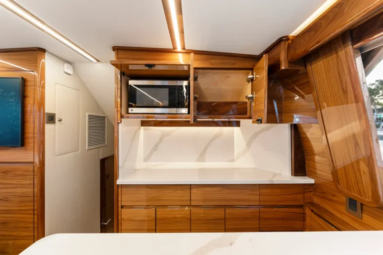 Wood-toned kitchen galley with built-in microwave in upper cabinet and white marble countertop beneath a glossy wood finish surface.