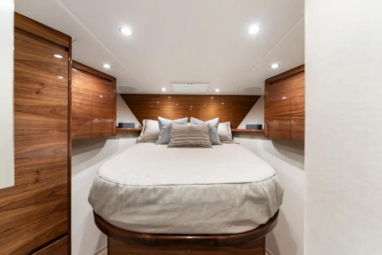 Luxurious wood-paneled bedroom with a round bed, multiple pillows, and built-in wardrobes along the sides in a yacht-like cabin.