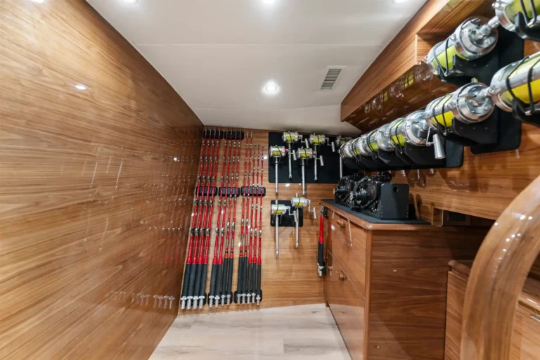 Row of fishing rods with reels stored vertically along a wood-paneled wall in a dedicated gear closet.