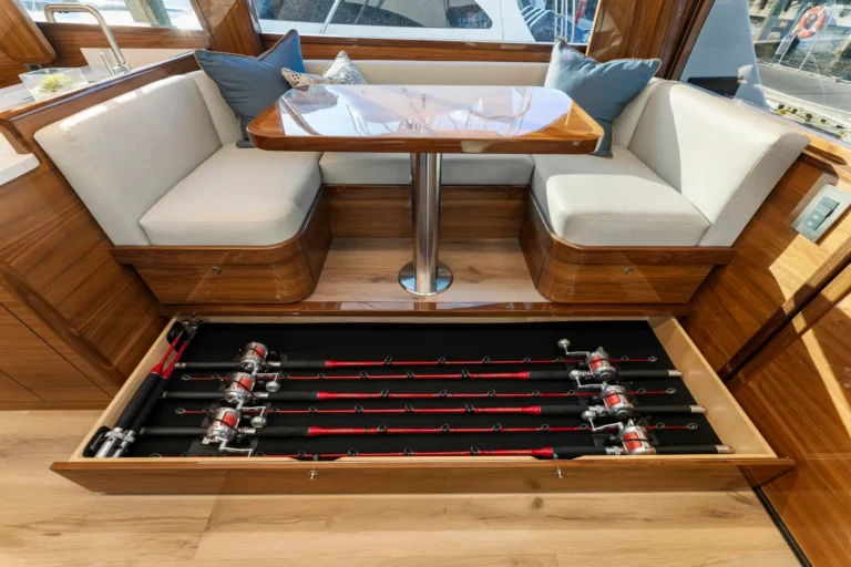 Boat cabin seating area with cream cushions and wood trim; an open drawer shows multiple fishing rods stored underneath the table.