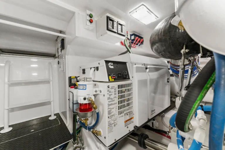 Marine engine room with a Cummins generator, control panel, and hoses in a white interior.