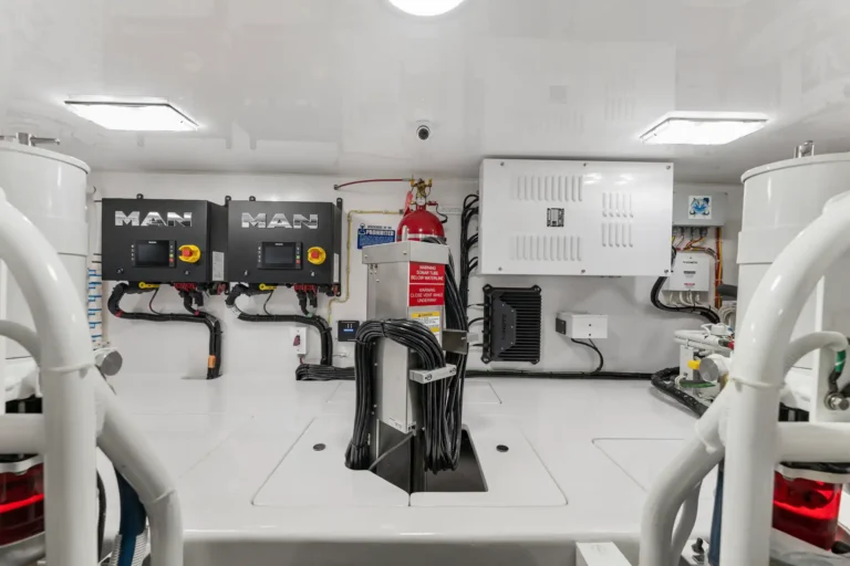 Marine engine/control room with two MAN control boxes, red emergency stop, and organized wiring on white walls.