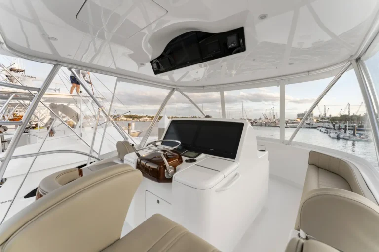 Boat cockpit with beige seats, steering wheel, and navigation screens overlooking a marina.