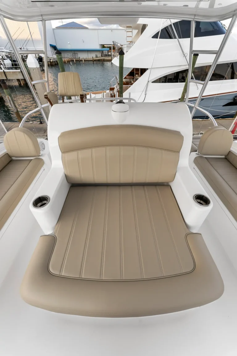 Beige-cushioned seating on a white yacht deck with a marina and other boats in the background viewed from the cockpit area