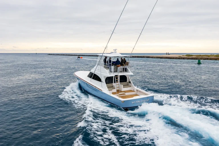 White motorboat with multiple passengers cruising through blue ocean, wake splashing behind the hull at sunset.