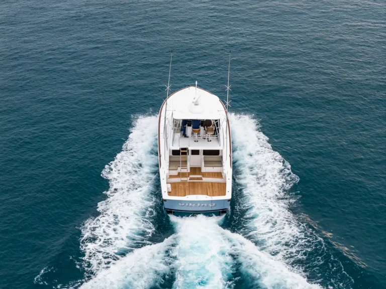 Top-down view of a white motor yacht sailing through deep blue water, leaving a foamy wake behind it.