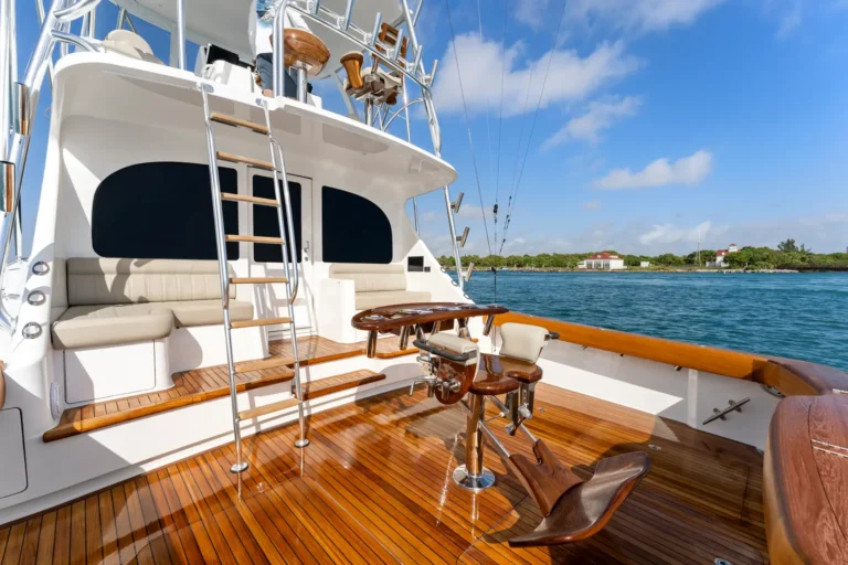 Luxury yacht deck with tan cushioned seating, wooden flooring, and metal ladder leading to upper level against a blue ocean backdrop.