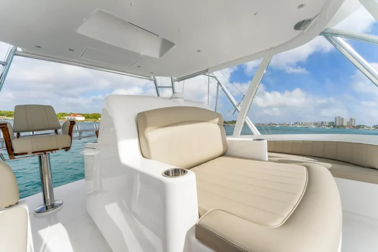 Luxury yacht cockpit with beige cushioned seats and cupholders, calm blue water beyond.