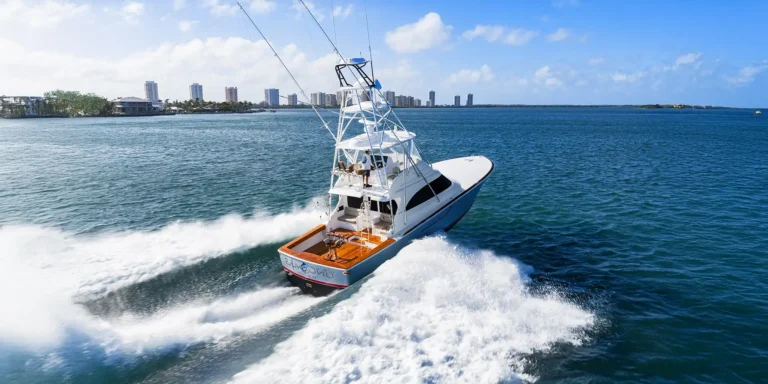 White speedboat skimming through blue water with a city skyline in the distance, under a clear sky.
