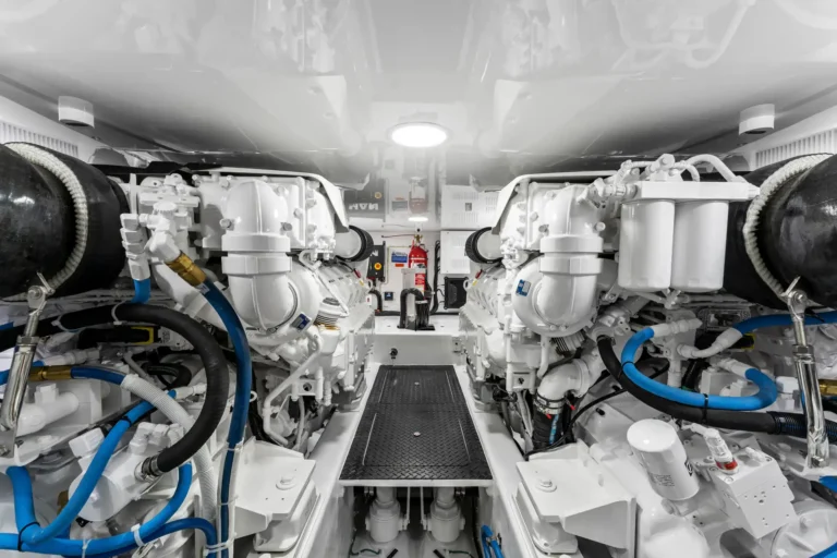 Interior of a white, well-lit engine room with large machinery on both sides and blue hoses running along the edges.