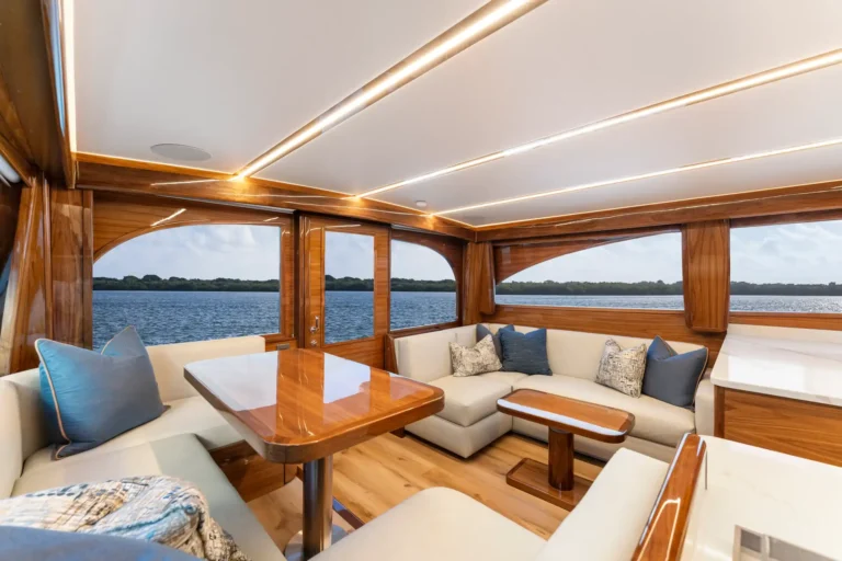 Luxurious yacht lounge with cream upholstery, blue pillows, and polished wooden tables overlooking the sea.