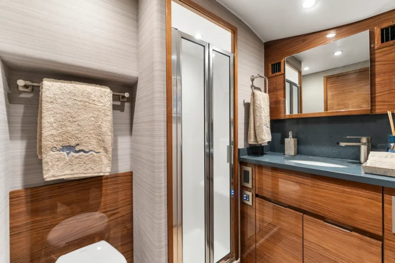 Bathroom interior with wood-tone cabinetry, gray countertop, sink, and beige towels on a wall rail.