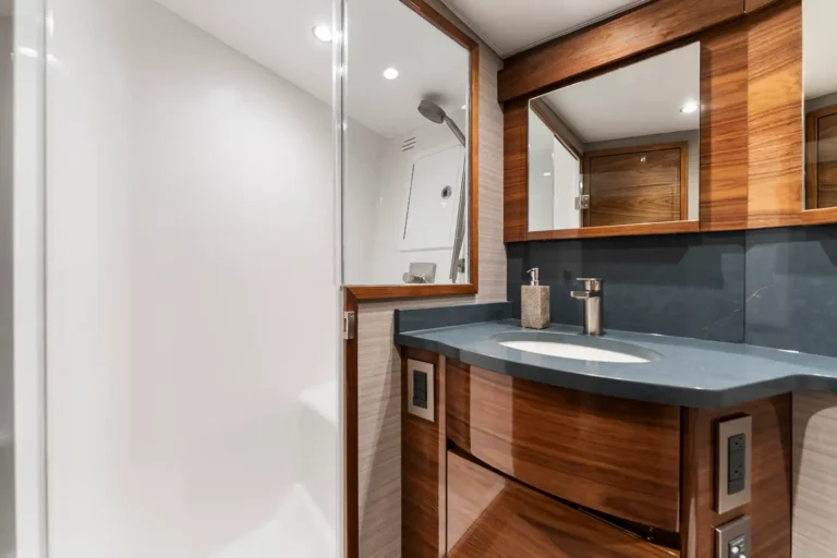 Modern bathroom vanity with wood-framed mirrors, gray countertop, oval sink, brass faucet, and soap dispenser in view.