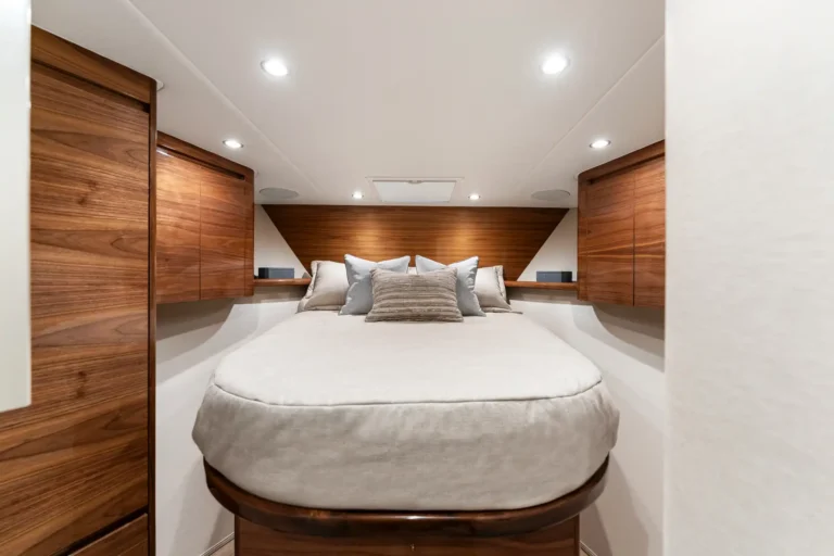 Cozy yacht cabin with a circular bed, soft beige linens, and warm wood cabinetry along the walls. Sheer, built-in lighting creates a calm atmosphere.