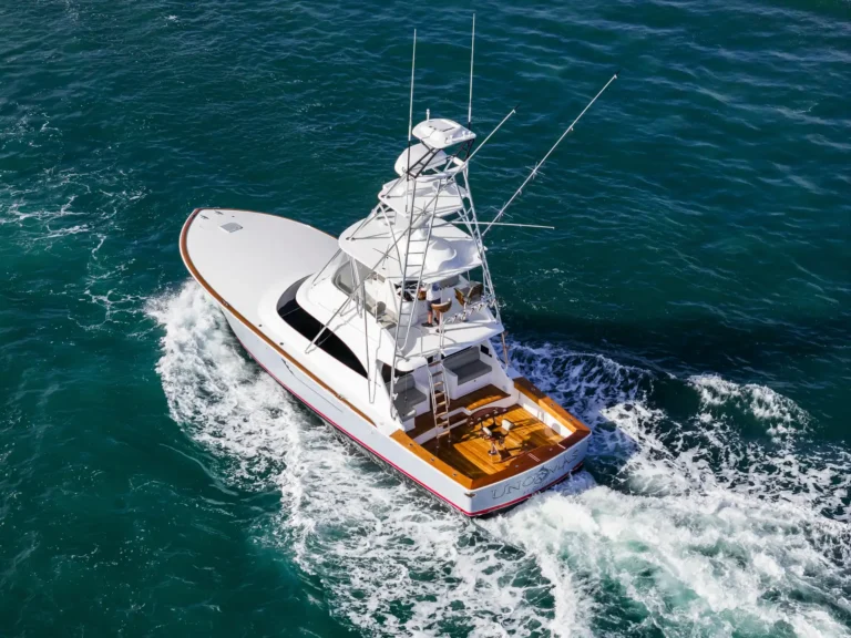 Aerial view of a white sport fishing yacht with a tall tower sailing through turquoise ocean waves, leaving white wake.