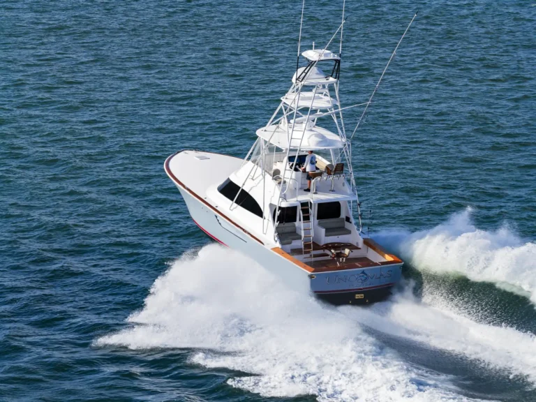 White multi-deck motor yacht speeds through blue ocean, leaving a large white wake behind.
