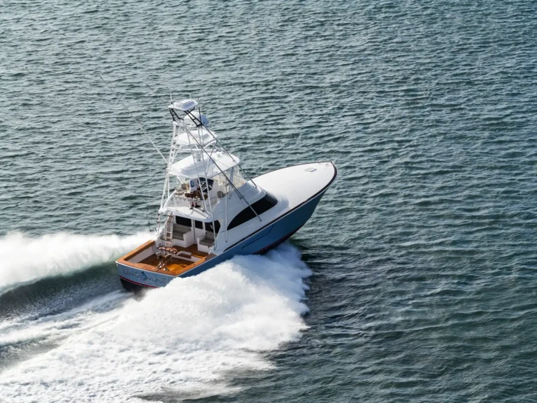 White motor yacht speeding through blue water, leaving a large white wake behind it.