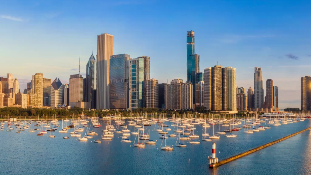 City skyline with tall skyscrapers along a harbor filled with sailboats.