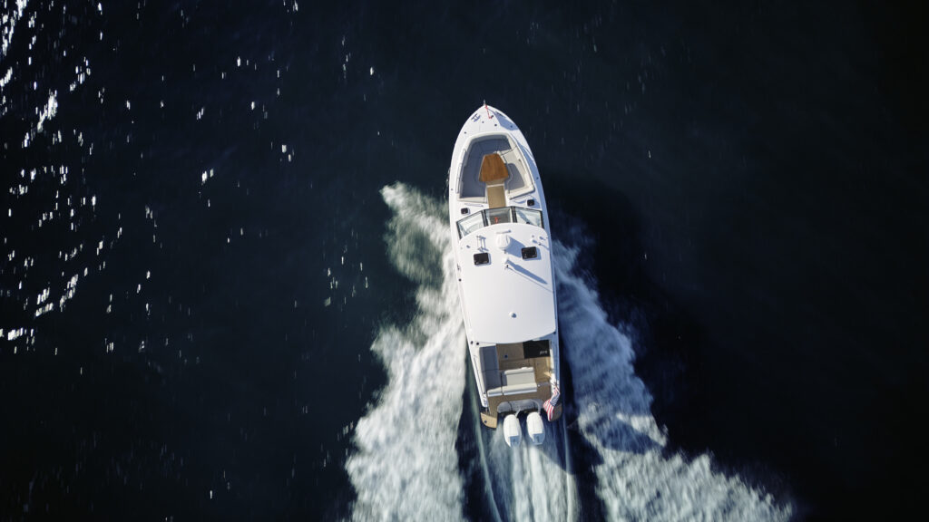 Top-down view of a white motorboat speeding through dark blue water with a white frothy wake behind it.