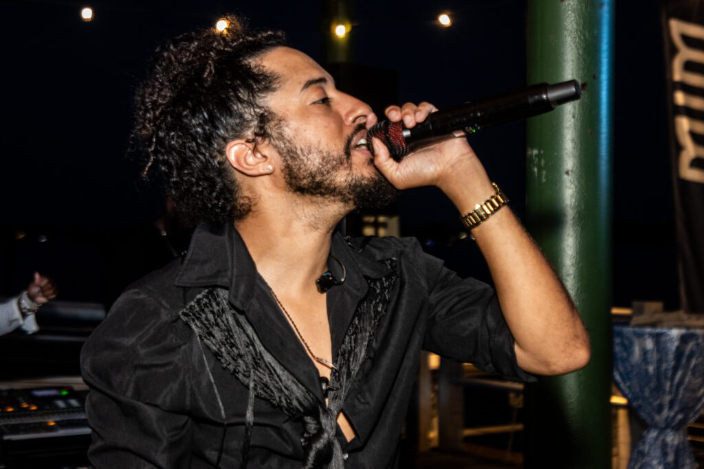 Male singer passionately singing into a microphone during a nighttime performance in a dark venue.