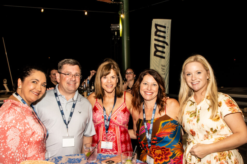 Five people posing for a nighttime group photo at a bar, wearing colorful outfits and name badges with drinks on the table in front of them.