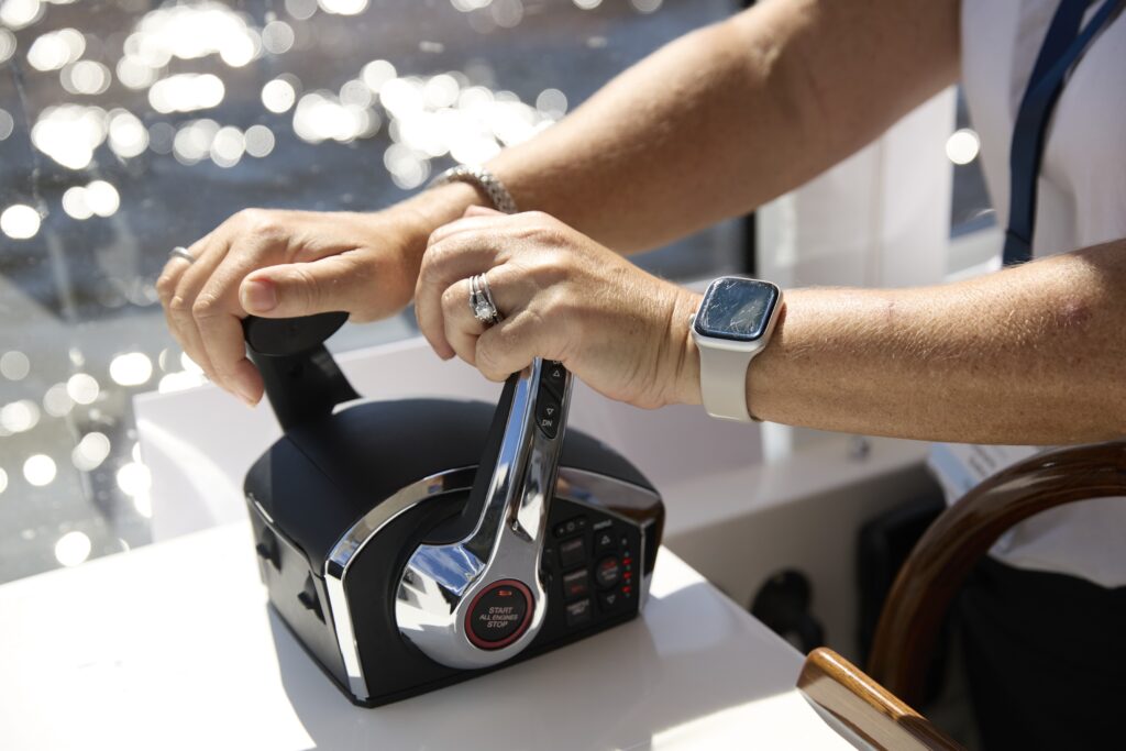 Two hands grip a car steering wheel; smartwatch on the right wrist and a ring on the left ring finger visible near the dashboard.
