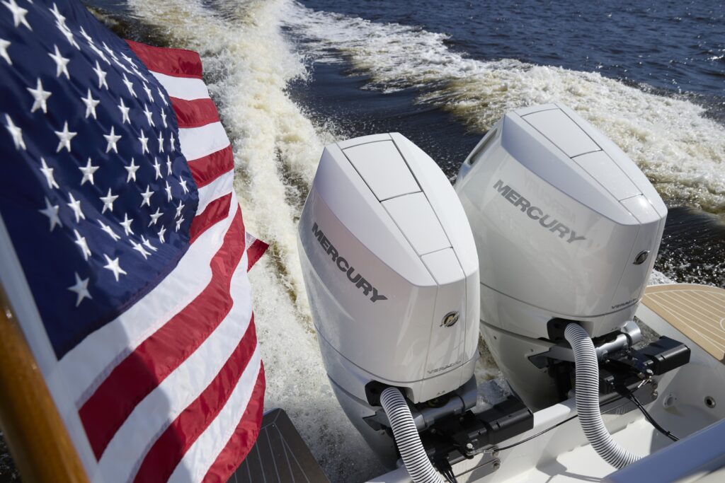 American flag waving at the stern of a speedboat with twin Mercury outboard engines cutting through waves